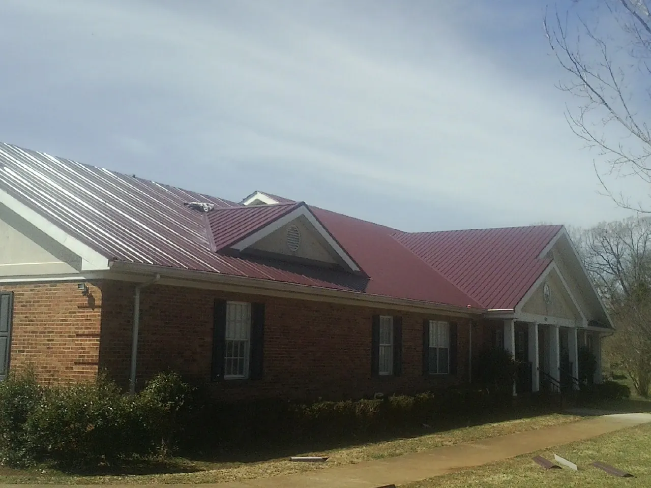Red metal roof with gabled entries on a long brick building, from a Hail Damage Roof Repair job in Canaan
