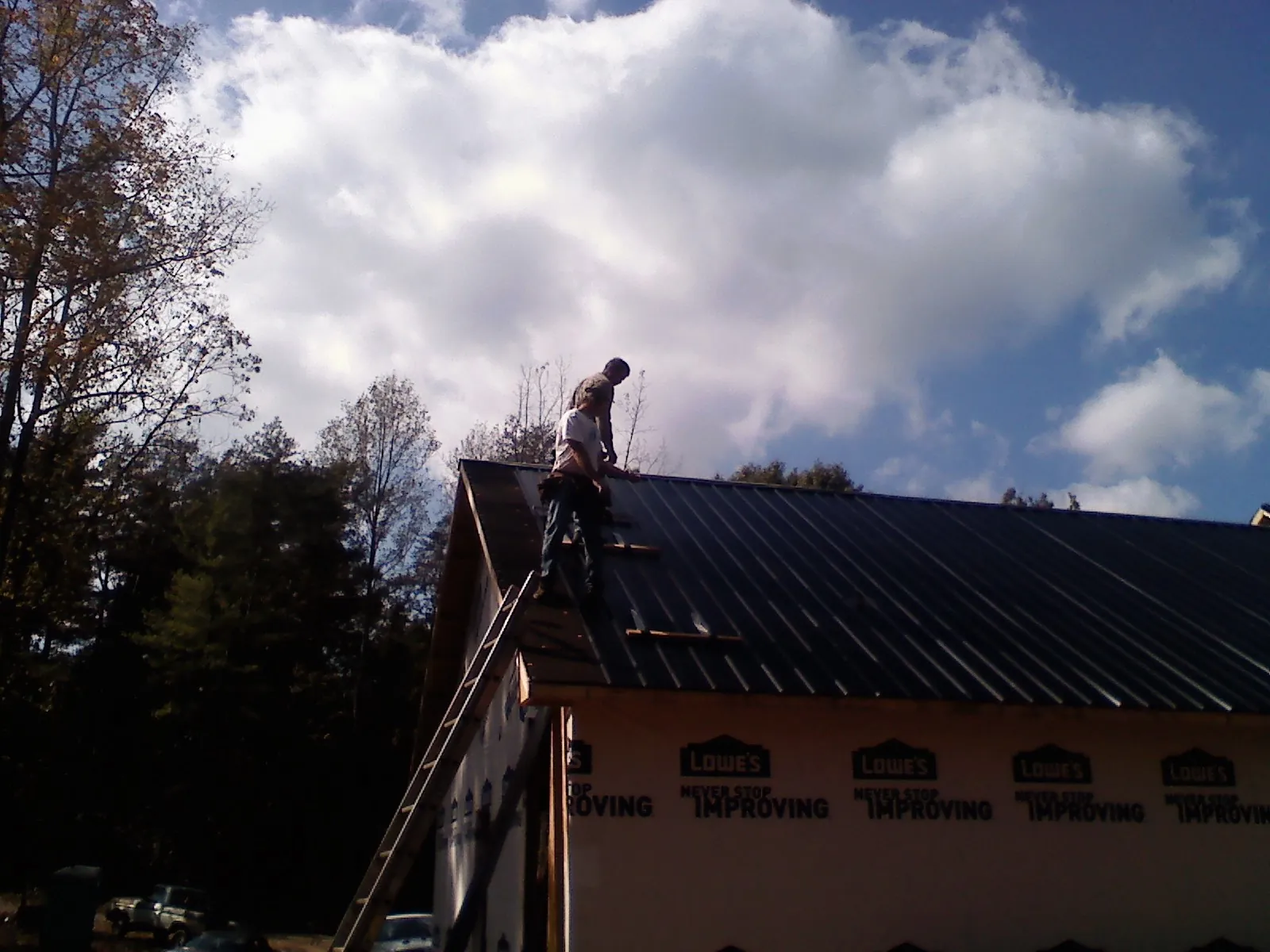 Roofer fastening dark metal panels high against a cloudy sky, from a Roof Inspection job in Canaan