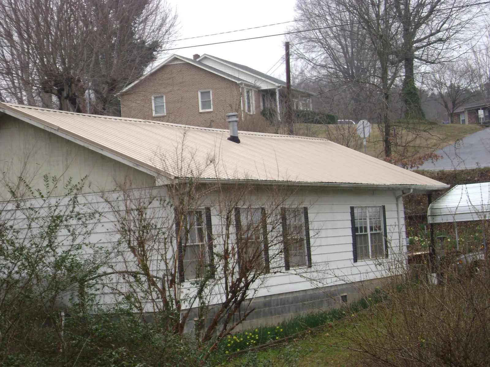 Tan metal roof on a white sided house set into a hillside — Commercial Roofing by Roofing Brothers in Canaan